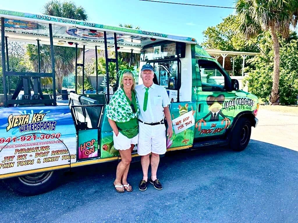 Riders aboard a green Frog Hop open-air trolley on Siesta Key