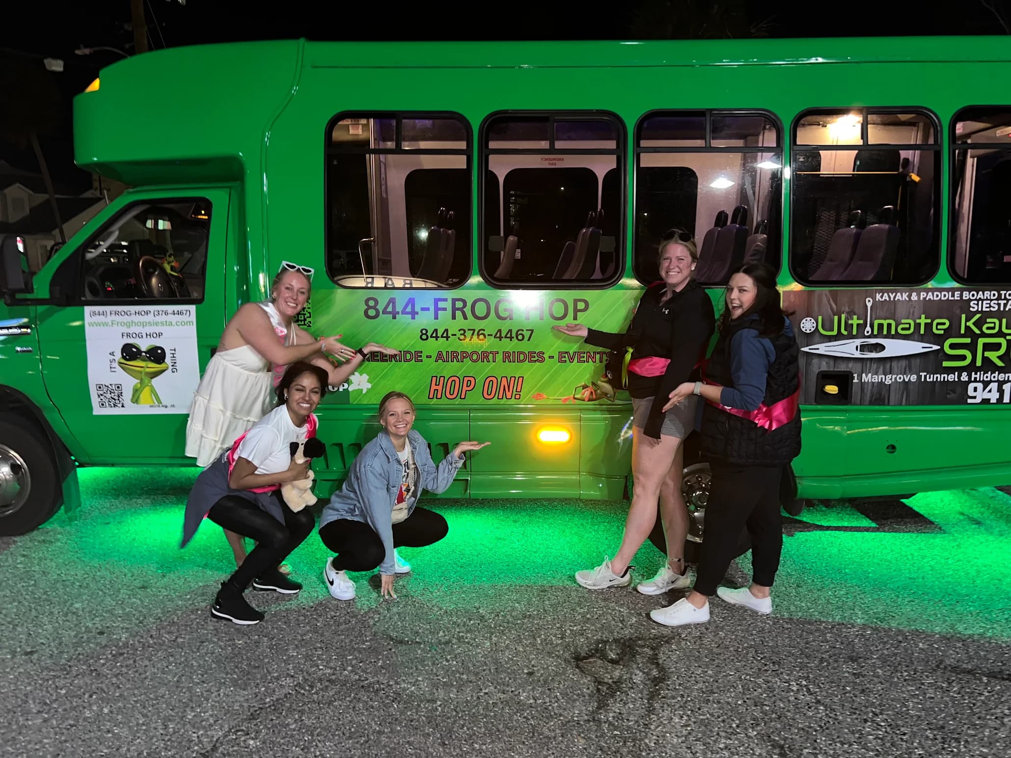 Riders posing beside the green Frog Hop bus lit up at night