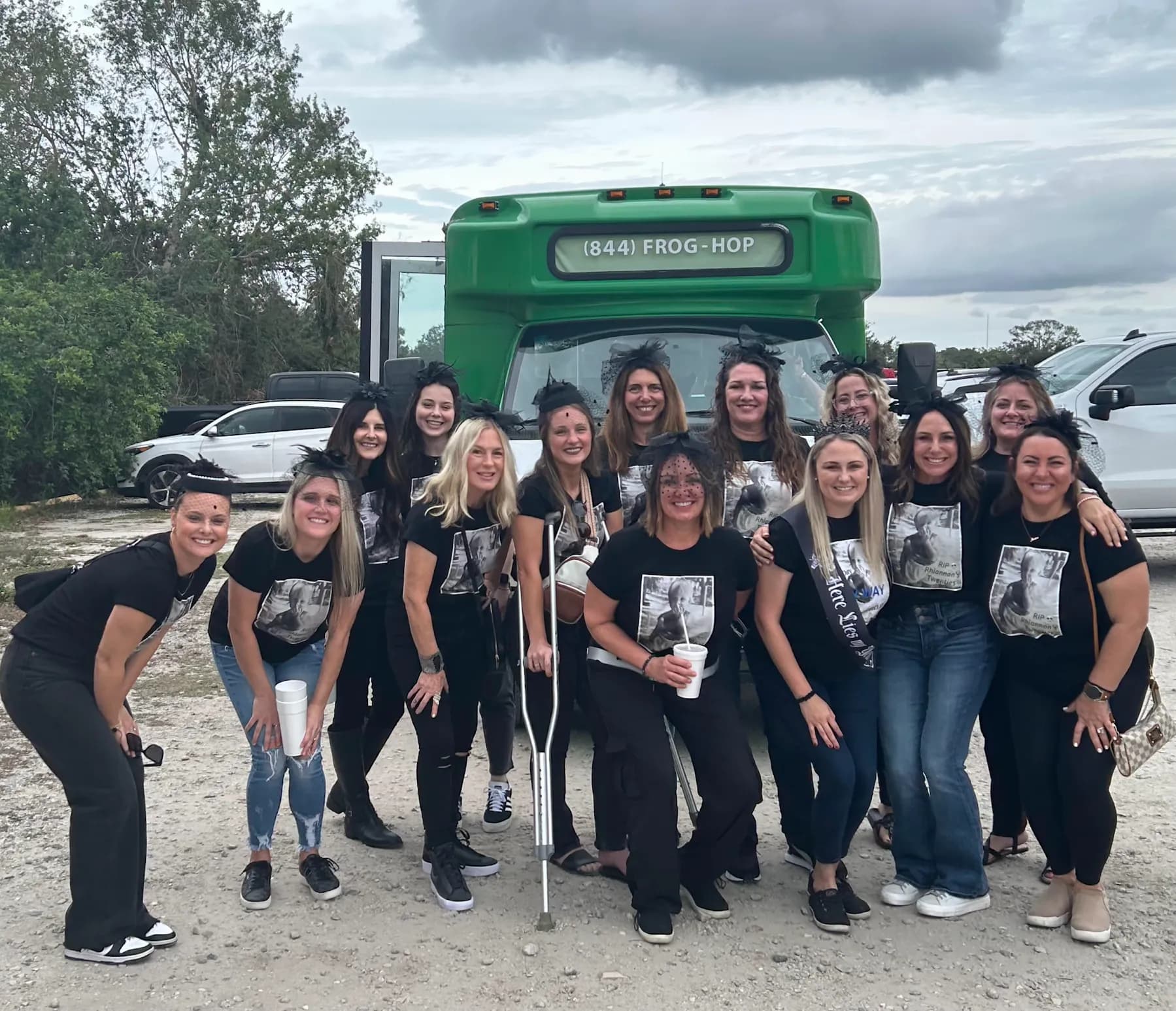 A big group of smiling riders posing in front of the green Frog Hop bus