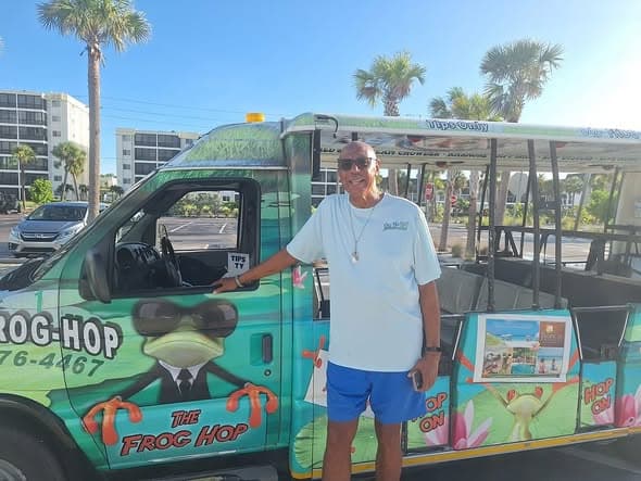A happy rider standing in front of a green Frog Hop trolley at the beach