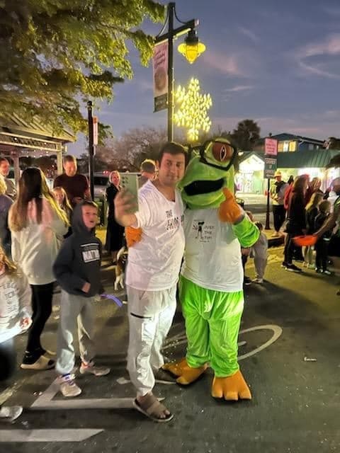 A rider posing with the Frog Hop frog mascot at a Siesta Key street festival